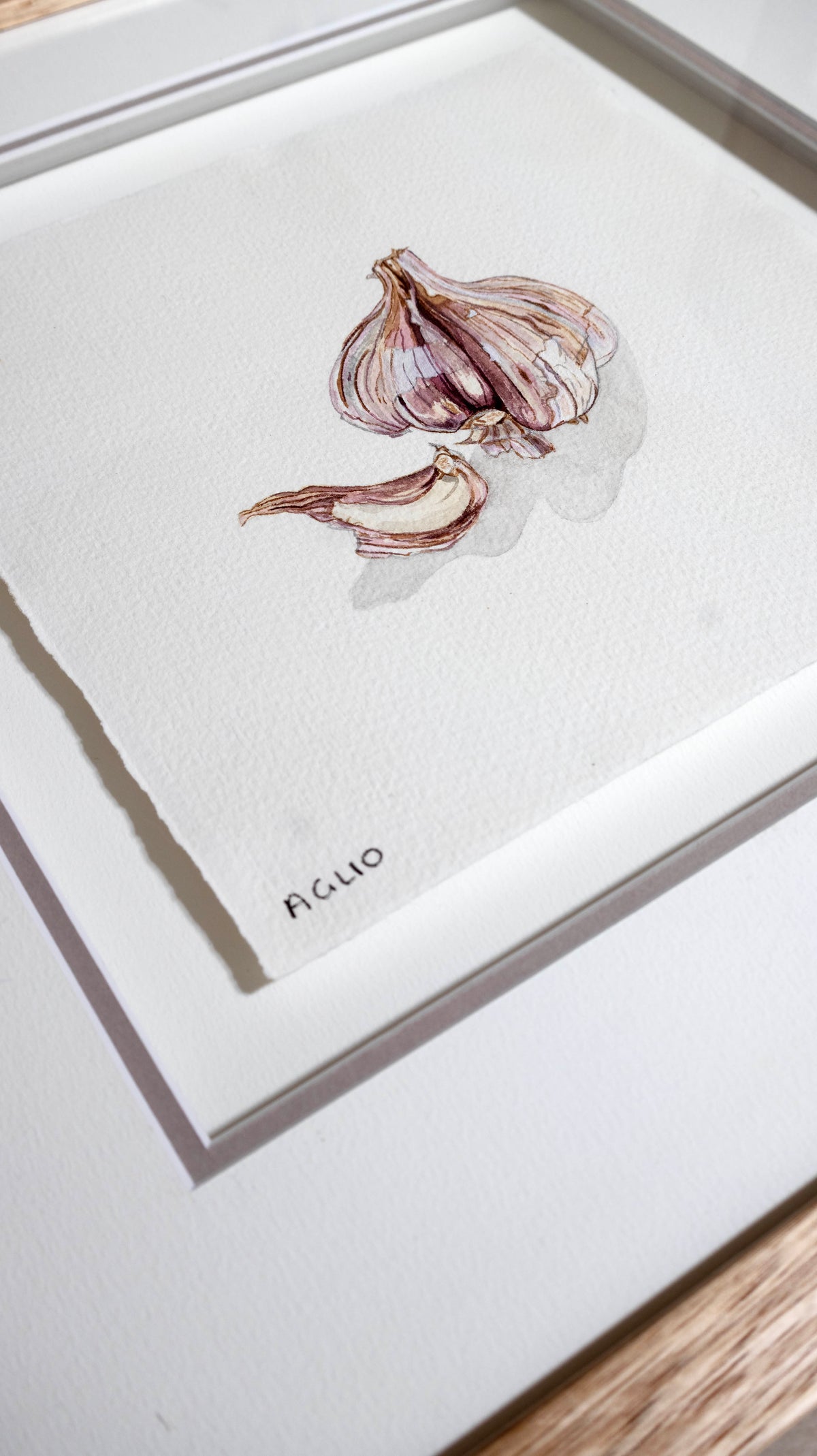 A framed watercolour art print featuring a painted garlic bulb and clove on a white textured background, with the word 'AGLIO' written in small black text near the bottom.