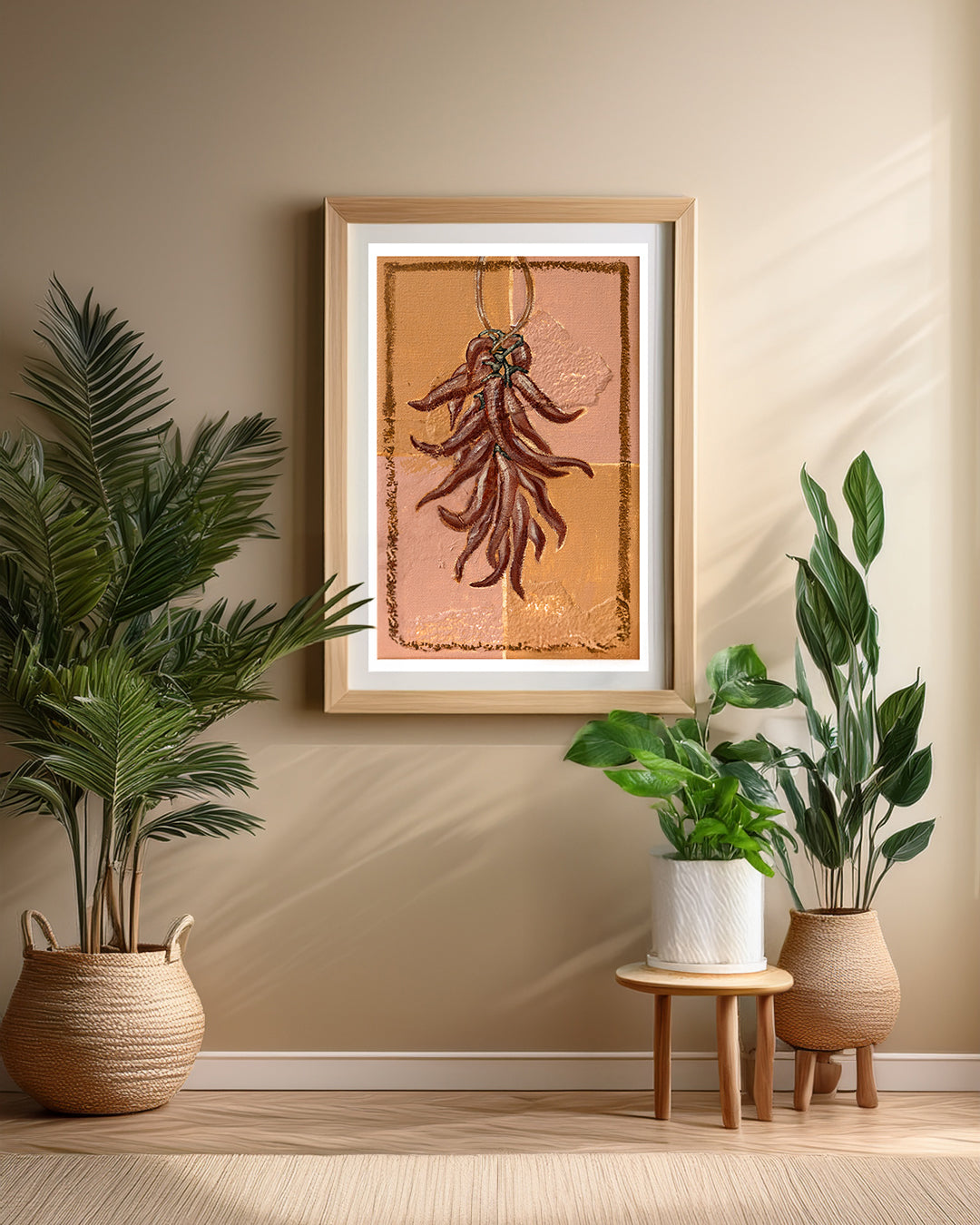 Chillies fine art print by Marissa Lico. Marissa Lico framed art print of dried chillies on a beige background, hung with plants and a stool below.