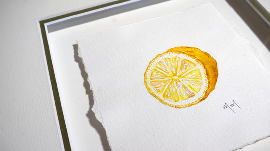 A square watercolor painting of a sliced lemon on textured white paper, mounted on a white mat board with a thin dark green matt edge visible. The painting is rendered in bright yellow tones with white highlights, and a small artist signature by Marissa Lico is visible in the lower right corner.
