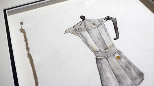 A framed watercolour-style painting of a moka pot, shown at an angle against a white mat and oak frame.