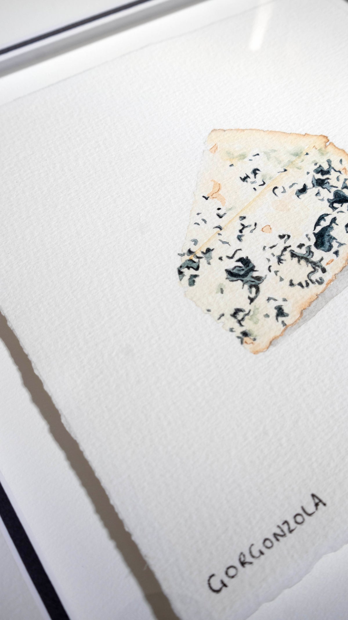 A close-up of a Gorgonzola cheese wedge on textured white paper, with the handwritten word 'GORGONZOLA' in the lower right corner.
