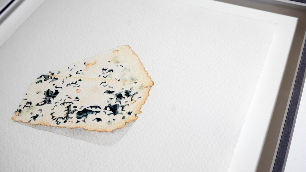 A single wedge of gorgonzola blue cheese on a white textured surface, photographed close up inside an oak light frame.
