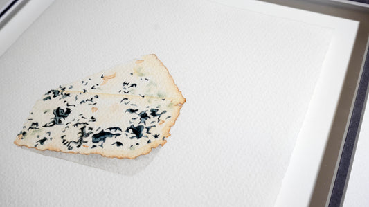 A single wedge of gorgonzola blue cheese on a white textured surface, photographed close up inside an oak light frame.