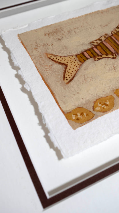 A close-up of framed wall art showing a textured beige background with a stylised fish motif in tan, brown, and muted orange, plus small decorative shapes near the bottom.