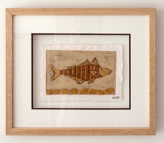 Framed folk artwork featuring a brown striped fish on a textured beige background, matted with white and housed in a light natural wood frame.