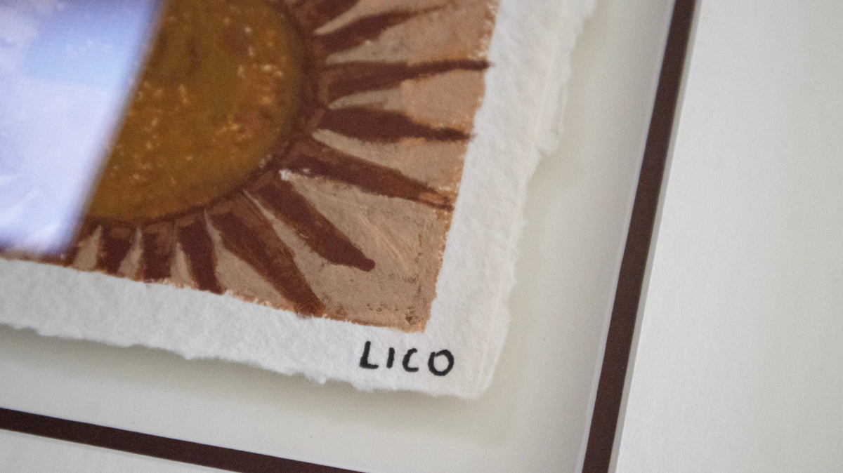 Close-up of a textured handmade paper original painting featuring a brown sun illustration, signed by the artist 'LICO' in black ink, floating in frame on a white surface.
