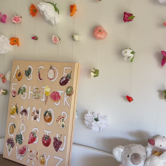 Alfabeto by Marissa Lico displayed in baby's nursery with hanging flower installation.